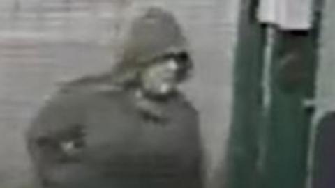 A blurry black and white image of a white man wearing a dark hooded jacket