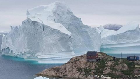An iceberg behind houses and buildings in Innarsuit, Greenland