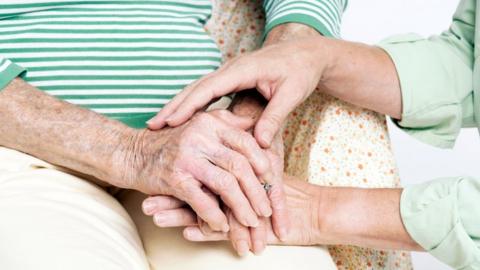 Elderly woman being comforted by a carer who is holding her hands.