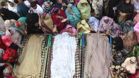 Muslim women and men gathered around three bodies in 2014