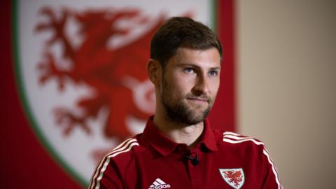 Ben Davies sits in front of the Wales badge