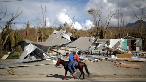 people ride a horse passed a destroyed building