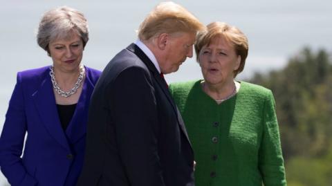 Theresa May and German Chancellor Angela Merkel look on as US President Donald Trump arrives for the family photo at the G7 Summit June 8, 2018