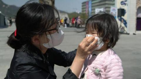 A woman helps a child put on a face mask in Seoul