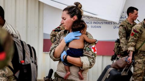 An Army paramedic holds a baby during evacuation of British nationals in Sudan