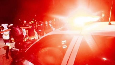 Protesters surround a police car at night with its red light flashing