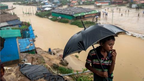 Boy with umbrella in front of flooded village