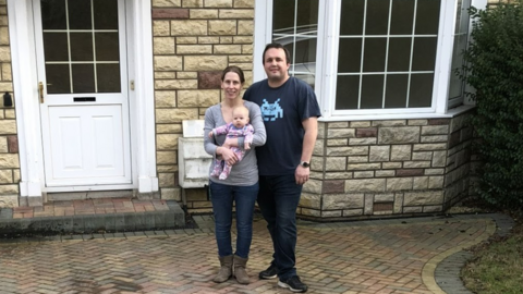 Simon and Louise walker holding their baby in front of their house