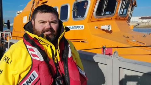 Robbie Maiden stands next to a lifeboat
