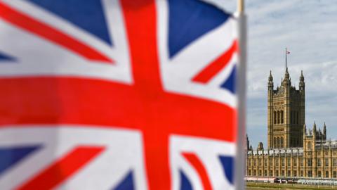 Houses of Parliament is seen from Westminster Bridge with a Union Flag in the foreground