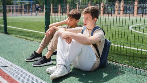 Young people looking bored while sat on a tennis court
