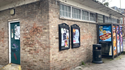 The outside of the toilet block showing walls with graffiti on and noticeboards