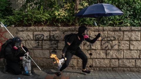 A masked protester - not the 12-year-old boy - holding an umbrella in one hand and a Molotov cocktail in the other