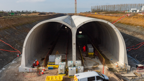 Double tunnel made out of concrete with construction site on both sides and workers within