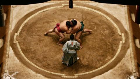 Sumo wrestlers Miyabiyama and Takekaze of Japan grapple each other in the middle of the ring during the Grand Sumo Championship