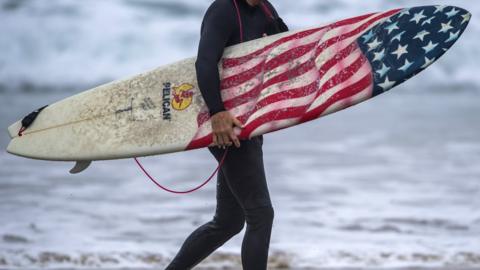 A surfer carries his patriotic board out of the water after surfing just south of the Newport Beach Pier in Newport Beach early Friday morning, September 7, 2018,