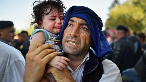 A man holds his crying child close to him as migrants force their way through police lines at Tovarnik station for a train to take them to Zagreb on September 17, 2015 in Tovarnik, Croatia.