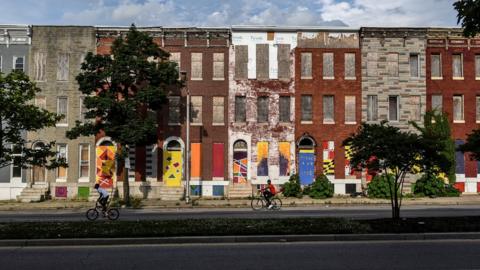 Young boys ride their bikes past a boarded-up and abandoned row of houses in Baltimore.