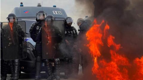 French gendarmes and CRS riot police stand on position near a fire as demonstrators gather on Place de la Concorde near the National Assembly to protest after French Prime Minister Elisabeth Borne delivered a speech to announce the use of the article 49.3, a special clause in the French Constitution, to push the pensions reform bill through the lower house of parliament without a vote by lawmakers, in Paris, France, March 16,