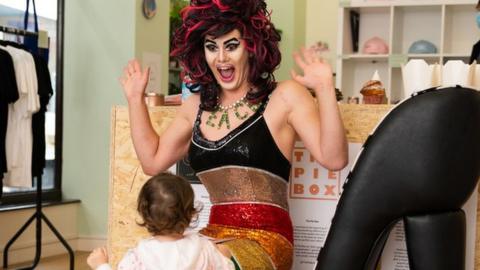 Aida H Dee The Storytime Drag Queen reading to children in a library.