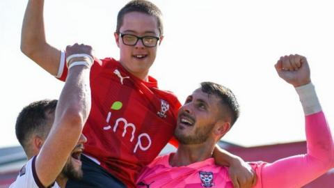 Jack Ratcliffe on the shoulders of York City's Olly Dyson and Peter Jameson