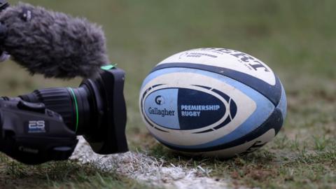 A TV camera points at a Premiership Rugby ball
