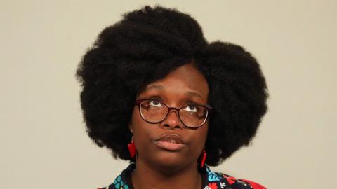 Sibeth Ndiaye looks up to the ceiling during a press conference from a podium