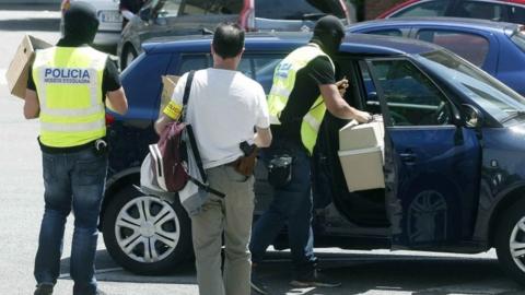 Police officers take away material seized during the raid