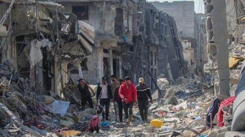 A group of people walking through rubble, outside destroyed buildings