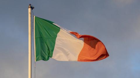 An Irish flag flies in the wind from a flagpole