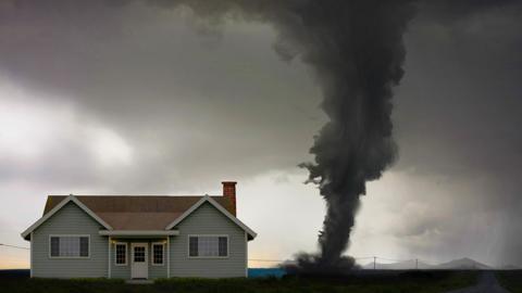 A dark tornado swirls near a house.