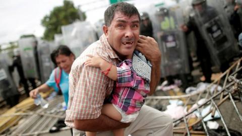 A Honduran man protects his baby amid clashes between migrants and Mexican Police