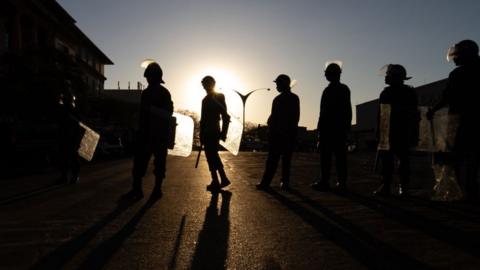 Silhouetted police officers in Zimbabwe bearing shields and batons