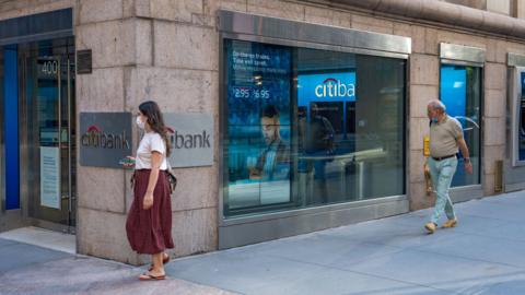 People in masks walk past a Citi ATM