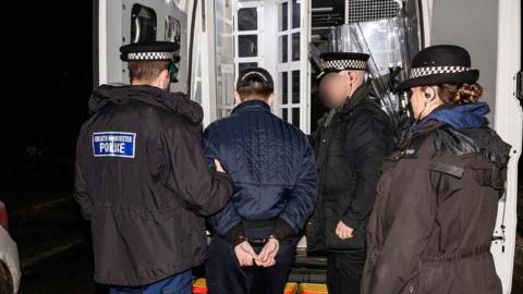 Police officers arrest a man and put him in a police van