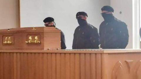 An image appearing to show masked men at a funeral at Roselawn Crematorium