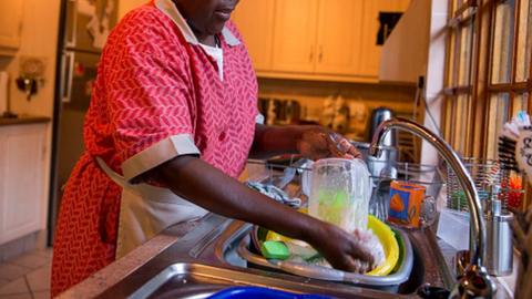 A domestic worker washes plates