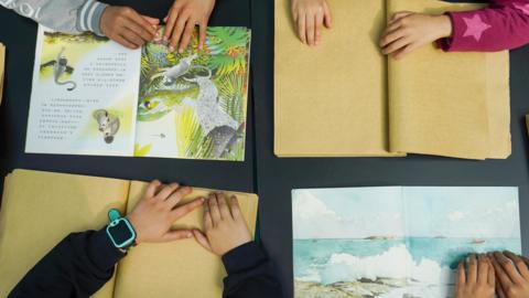 Four open books with children's hands resting on them
