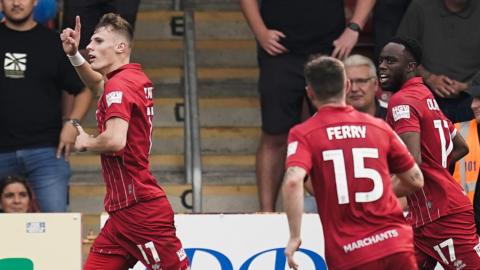 Rob Street (left) runs with his hand in the air as he celebrates his goal for Cheltenham