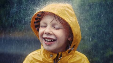 Little boy in raincoat smiles as it rains