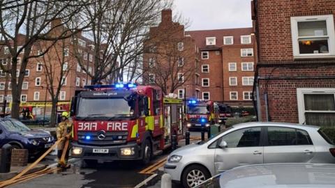 Image of several fire engines with blue lights parked outside blocks of flats