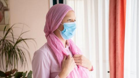 Female cancer patient, wearing a mask and a headscarf (stock photo)