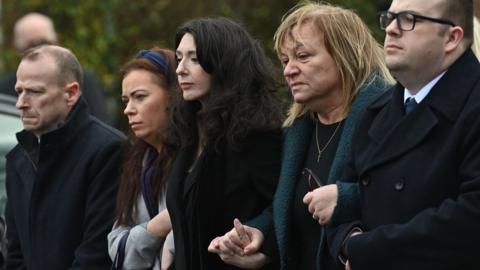 Mr Stalford's wife, motehr and family hold hands behind the hearse