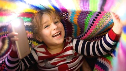 Boy with a smartphone under a blanket