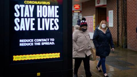 Two women walk past a stay home sign in Hyde, Greater Manchester