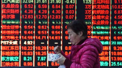 A woman walks part stock market board in China