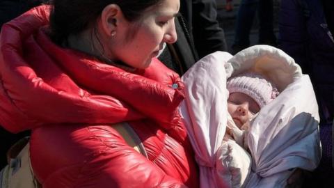 A woman holds her baby wrapped in a pink blanket at the Medyka border crossing from Ukraine to Poland in March 2022