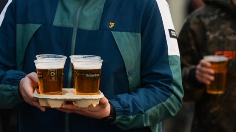 Men carrying takeaway pints in plastic glasses