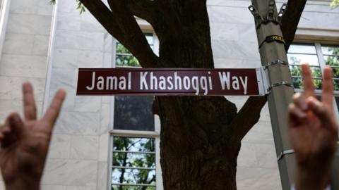 Activists give v-signs in front of the street sign for Jamal Khashoggi Way in Washington DC (15/06/22)
