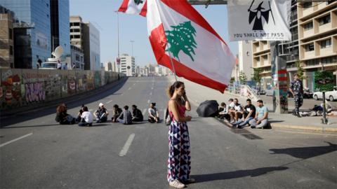 A woman holds a Lebanese flag at a roadblock put in place by anti-government protesters in Beirut, Lebanon